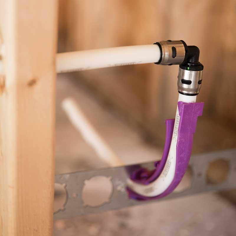 PEX plumbing pipe supported with a purple HoldRite pipe support bracket inside a wall 